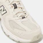 White athletic sneaker close-up of the toe area with mesh upper, stitched overlays, and laces visible.