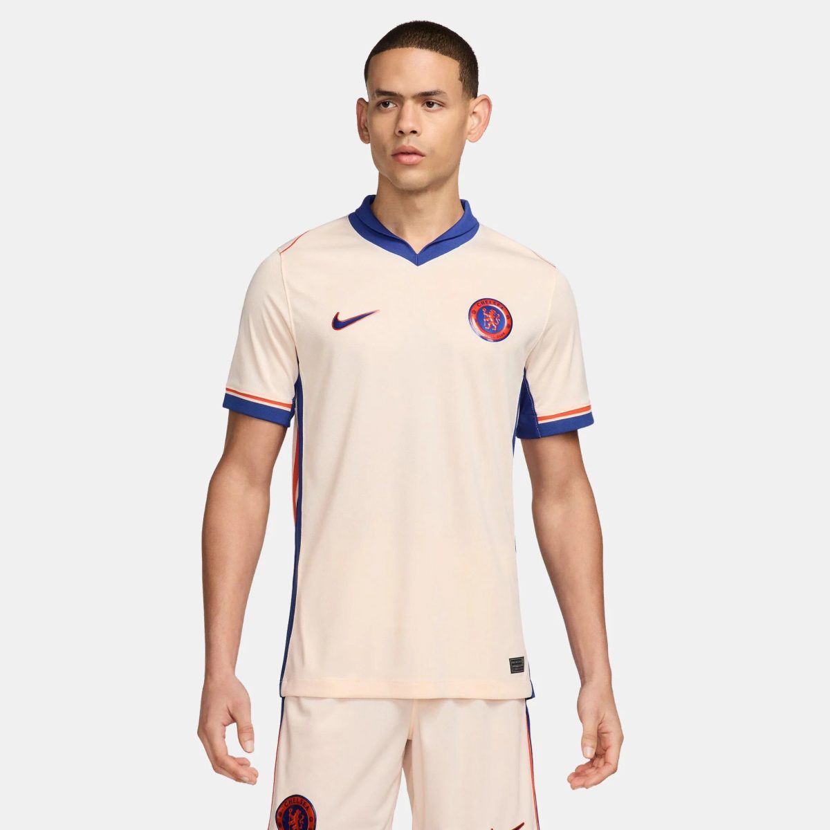 Male model wearing a cream Chelsea FC football jersey with blue trim and crest visible on chest edge.