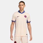 Male model wearing a cream Chelsea FC football jersey with blue trim and crest visible on chest edge.