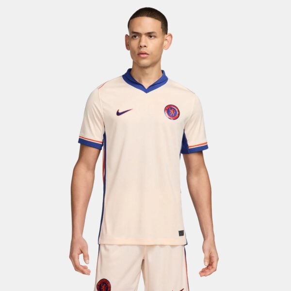 Male model wearing a cream Chelsea FC football jersey with blue trim and crest visible on chest edge.