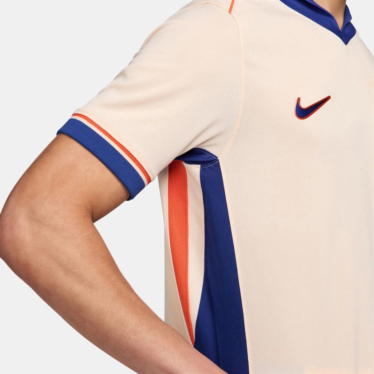 Close-up of a beige polo shirt with blue and orange trim; a blue Nike swoosh logo is visible on the chest.