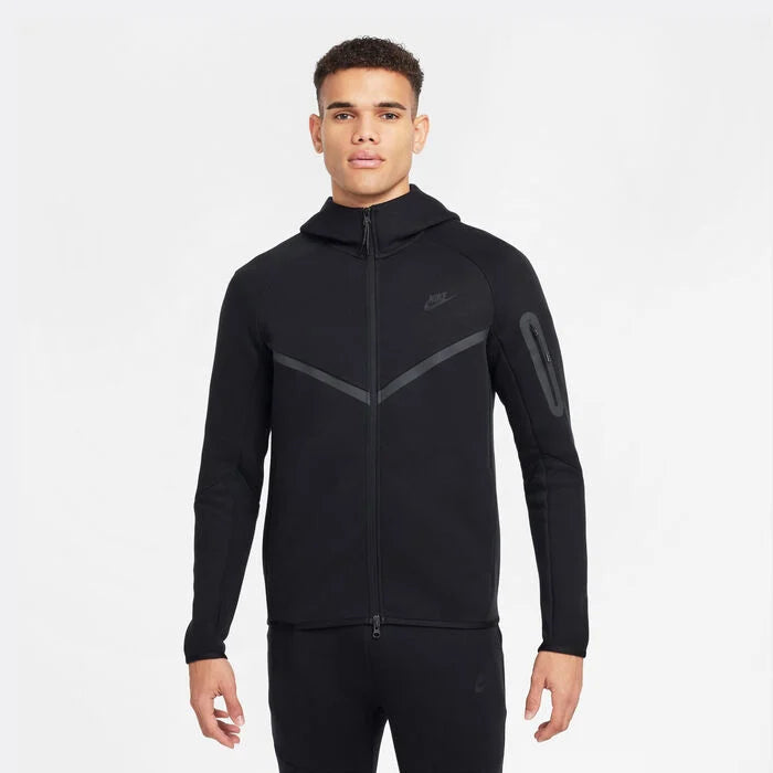 SSS2_NKHV0949_010_197602922080_1 Front view of a man wearing a black Nike zip-up hoodie with a high collar and reflective chevron design across the chest and a zip pocket on the left sleeve.