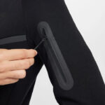 Black jacket sleeve with a vertical zip pocket; a hand pulls the zipper cord.