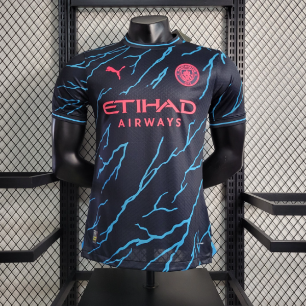 Manchester City football jersey on a mannequin: black with blue lightning stripes, pink Etihad Airways logo, Puma logo, and club badge visible.
