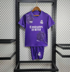 Purple Real Madrid soccer jersey with matching shorts hanging on a hanger in a black metal rack; features Emirates Fly Better slogan and club crest, with faint rose patterns on the shirt.