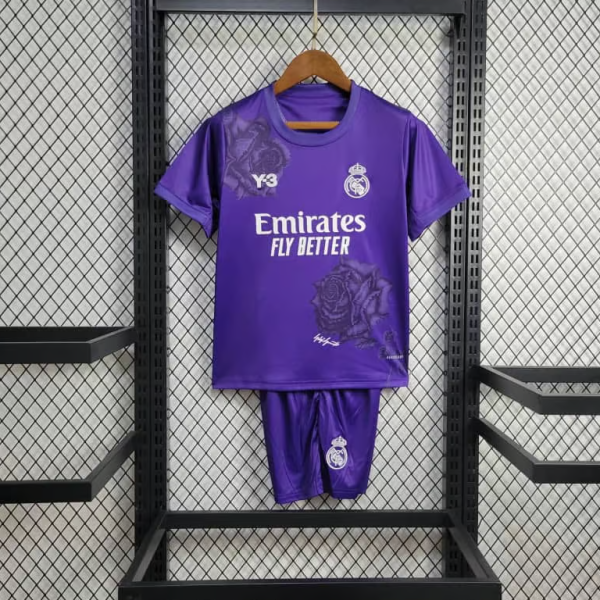Purple Real Madrid soccer jersey with matching shorts hanging on a hanger in a black metal rack; features Emirates Fly Better slogan and club crest, with faint rose patterns on the shirt.