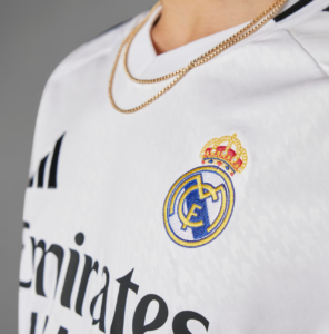 Close-up of a white Real Madrid jersey displaying the club crest and a gold chain around the neck.
