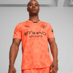 Man wearing a bright orange Manchester City jersey with Etihad Airways sponsor, posing from the chest up indoors.