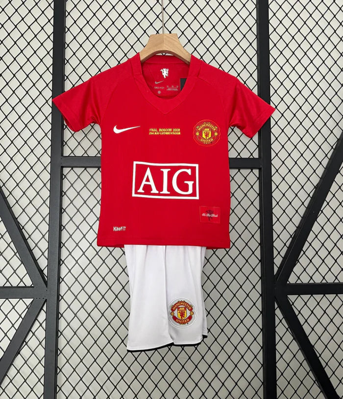 Screenshot2024-12-04at14.01.30_700x_5ada350e-1302-4fcb-9810-c46499429fd1 | UAE SPORT STORE Red Manchester United football jersey on a hanger with white shorts, displayed against a lattice backdrop, featuring the AIG sponsor logo and club crest on the chest.