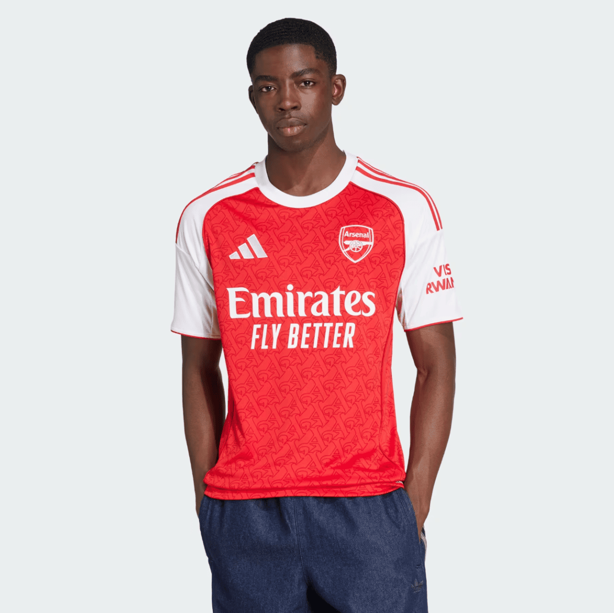 Young man modeling an Arsenal away jersey (red body, white sleeves) with the 'Emirates Fly Better' slogan.
