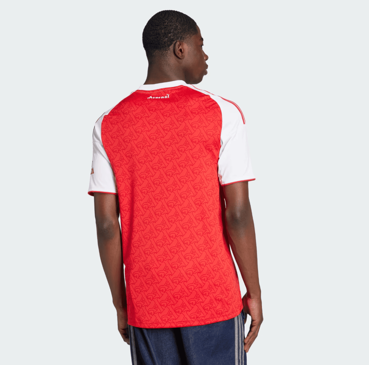 Back view of a person wearing a red Arsenal football jersey with white sleeves against a light gray background.