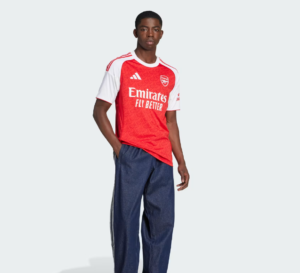 Man modeling an Arsenal football jersey (red with white sleeves) paired with dark blue jeans, posing confidently against a light background.
