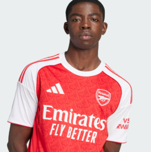 Portrait of a young man facing the camera, wearing a red and white Arsenal jersey with the Emirates Fly Better sponsor and crest visible.