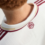 Close-up of a white sports jersey collar with burgundy and gold trim and a small geometric crest on the back.