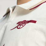 Close-up of a white polo shirt with a maroon embroidered emblem resembling a wheel and wing.