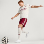 Soccer player in a white jersey and maroon shorts kicking a soccer ball on a plain background.