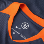 Close-up of a navy jersey with bright orange collar trim; white Nike swoosh, circular '90' emblem, and DRI-FIT ADV text visible.