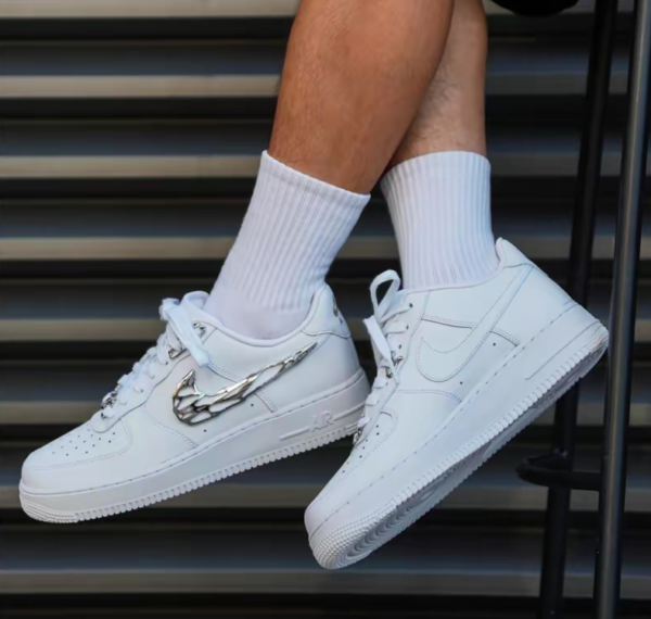 Pair of white Nike sneakers with a chrome wing design on the side, worn with white crew socks, resting on metal steps.