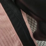 Close-up of a pink textured fabric strap adjacent to a black garment, with a grid-pattern background visible behind.