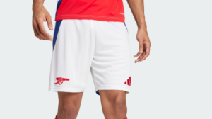 White athletic shorts with a red Arsenal cannon logo on the left leg and a red three-stripe mark on the right leg, worn with a red jersey.