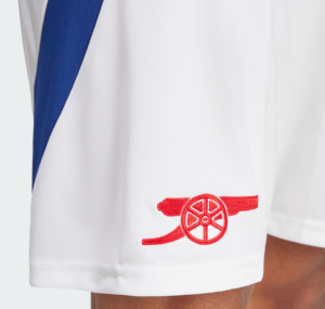 Close-up of white fabric with a red cannon logo embroidered near the hem, likely part of a sports uniform shorts
