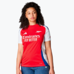 Female model wearing Arsenal away jersey: red body, white sleeves, blue side panels, Emirates Fly Better logo.