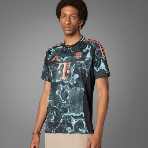Young man wearing a navy teal tie-dye Adidas Bayern Munich soccer jersey with orange accents and sponsor logo.
