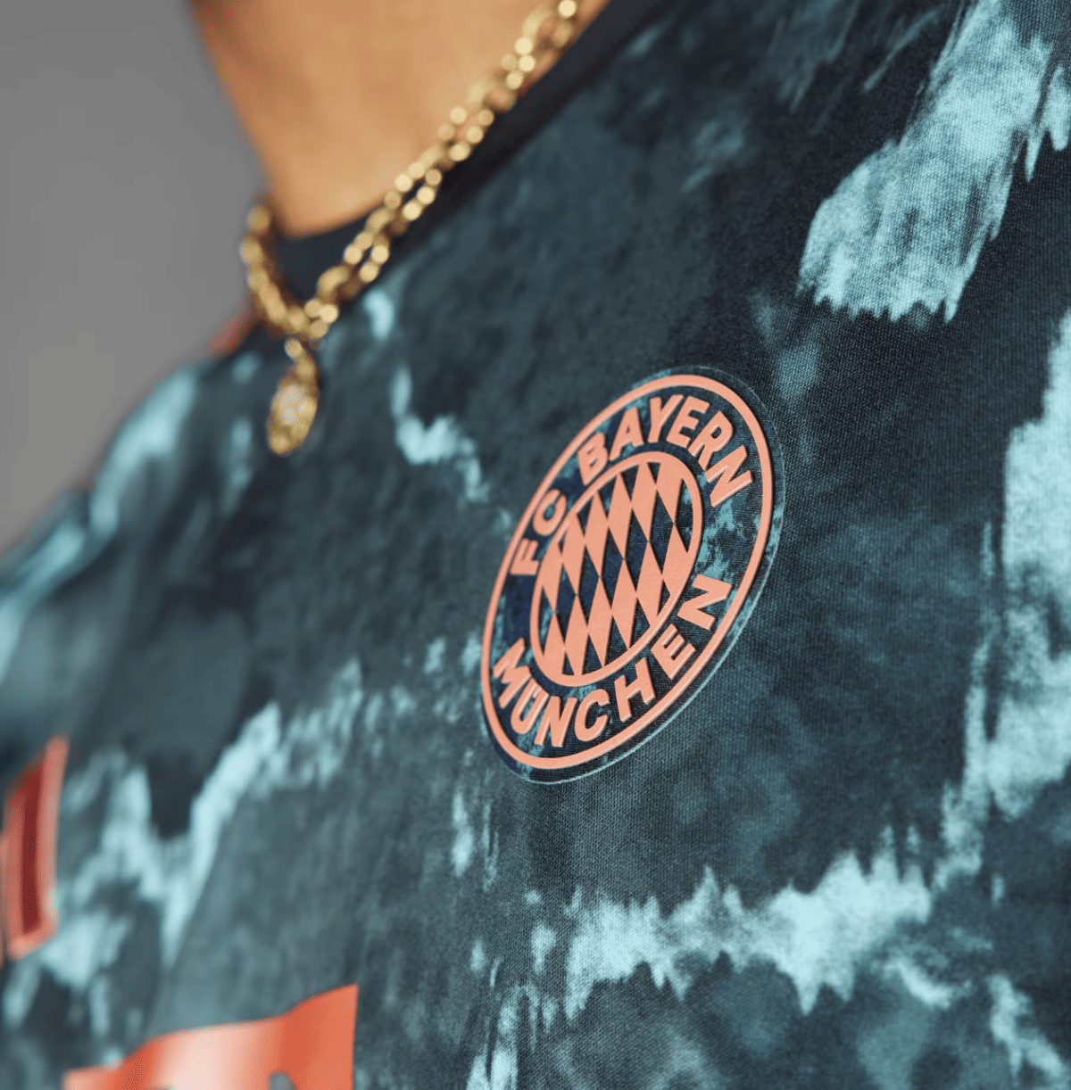 Close-up of a teal tie-dye shirt with a peach FC Bayern Munich badge on the chest.
