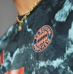 Close-up of a teal tie-dye shirt with a peach FC Bayern Munich badge on the chest.