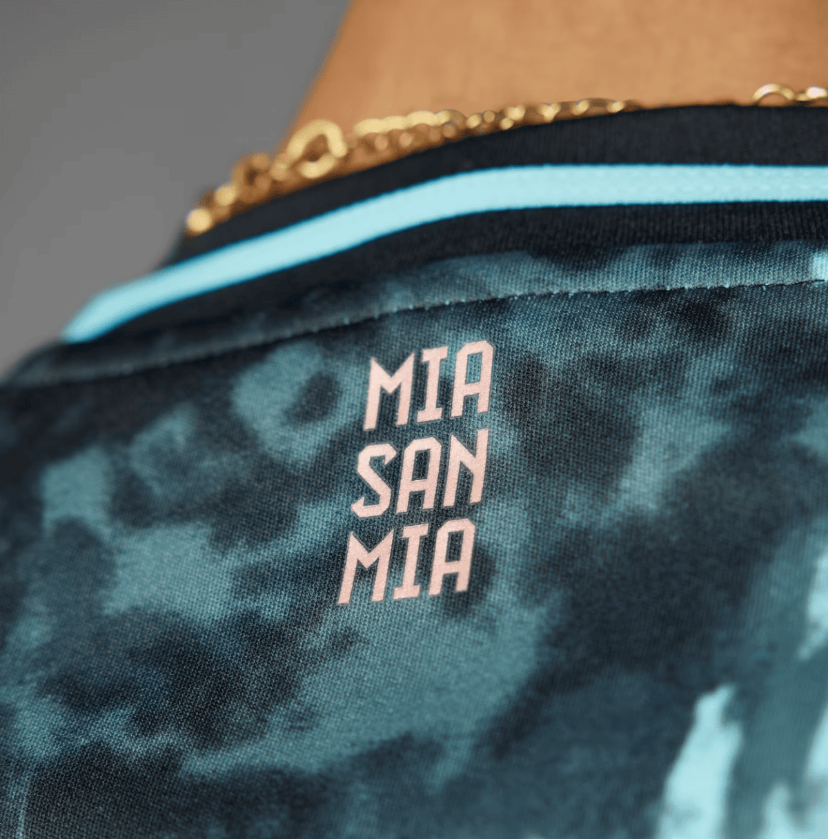Close-up of a teal camouflage bag with pink stacked text reading 'MIA SAN MIA'.