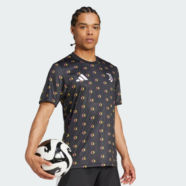 Soccer player wearing a black training jersey with colorful circular pattern, holding a soccer ball at his side.