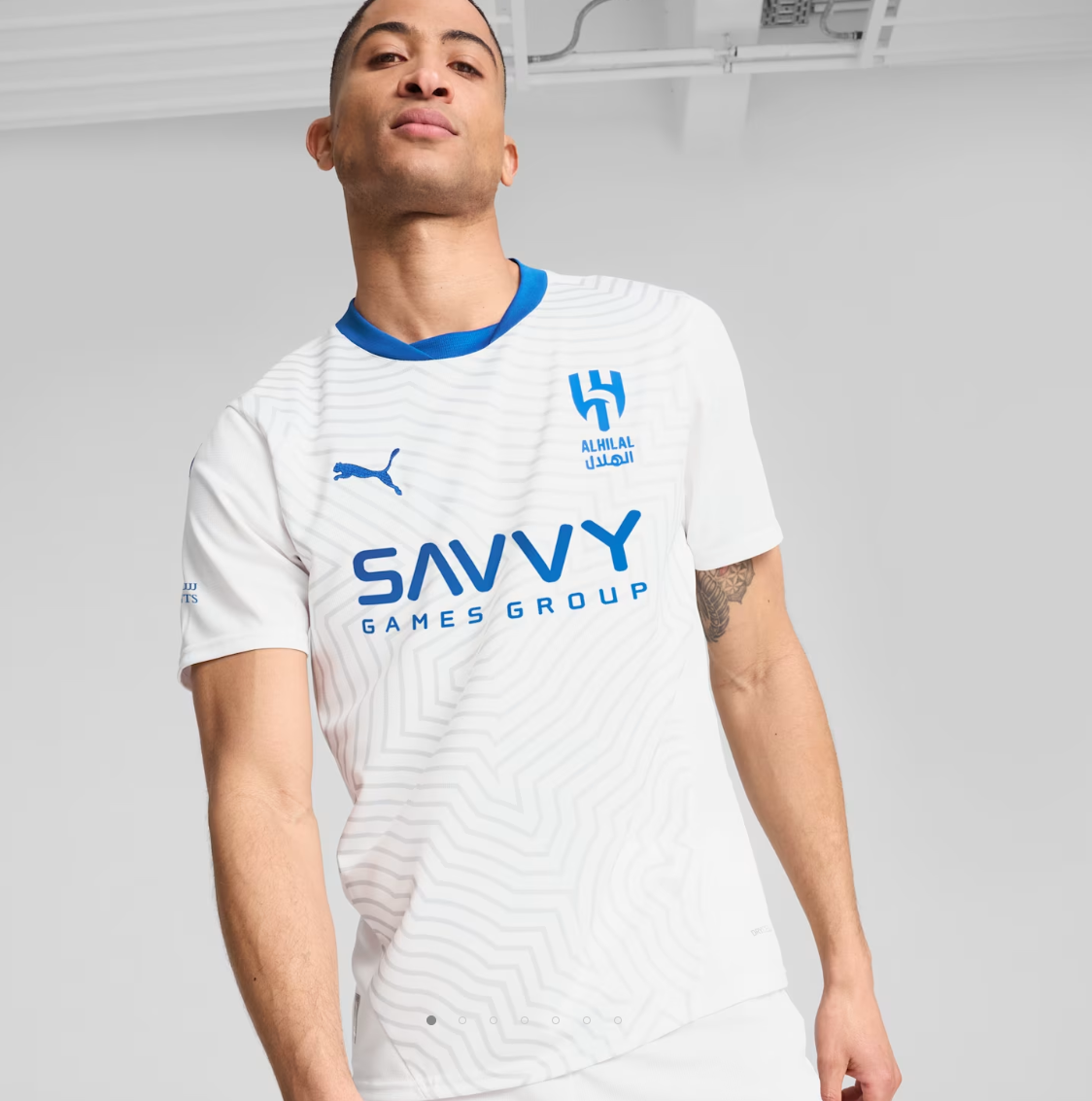 Screenshot_2024-09-04_203240 | UAE SPORT STORE Male model wearing a white sports jersey with blue logos, featuring the Savvy Games Group emblem on the chest in a studio setting.