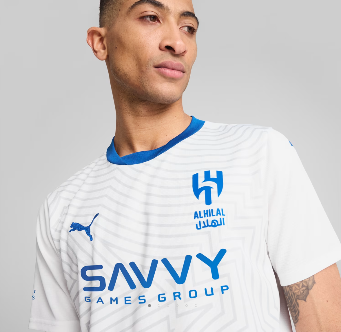 Screenshot_2024-09-04_203249 | UAE SPORT STORE Portrait of a person in a white jersey with blue accents and logos (SAVVY Games Group, Al Hilal, Puma) showing branding details on chest and sleeve edge.