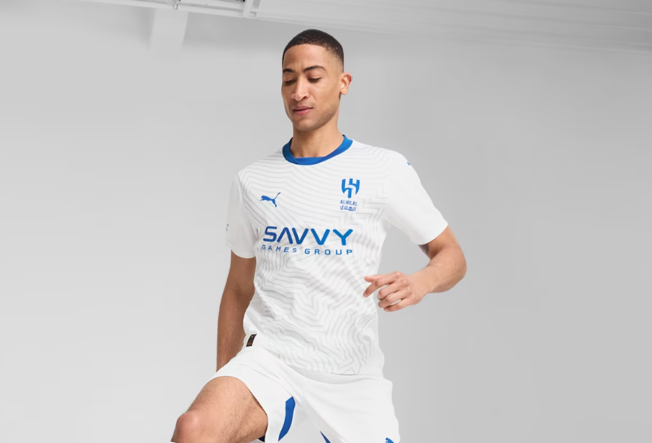 Screenshot_2024-09-04_203255 | UAE SPORT STORE Male soccer player in a white kit with blue accents, mid-stride and running, Savvy Games Group logo on the chest.