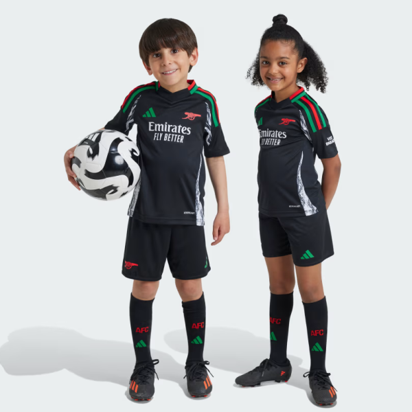 Two children in black Arsenal youth soccer kits stand side by side, one holding a soccer ball against a light background.