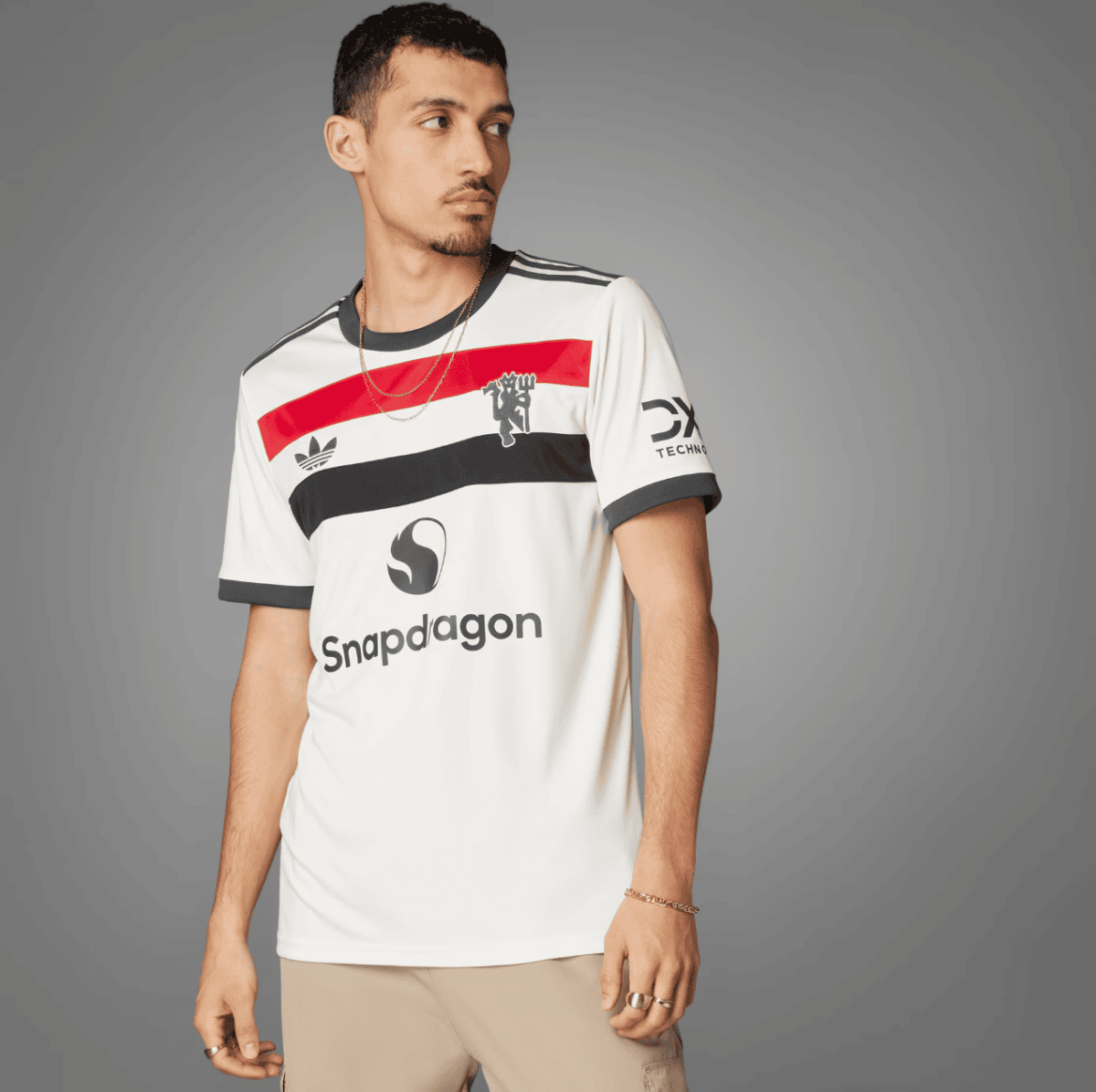 Man posing in a white jersey with red and black stripes, Snapdragon logo, against a gray backdrop.