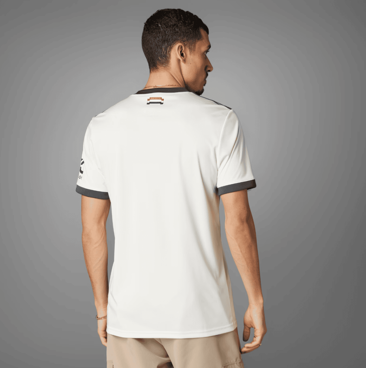 Back view of a man wearing a white polo shirt with dark gray sleeve cuffs and a small neck label, standing against a gray studio backdrop.