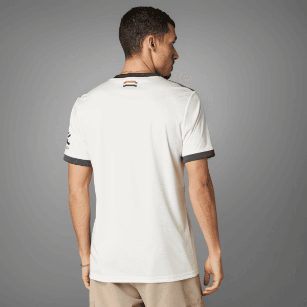 Back view of a man wearing a white polo shirt with dark gray sleeve cuffs and a small neck label, standing against a gray studio backdrop.