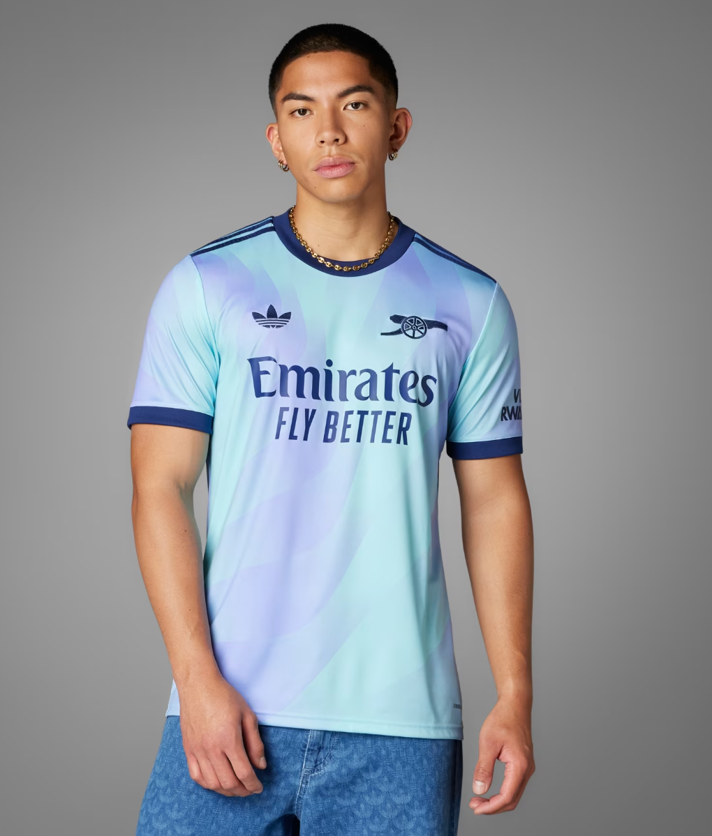 Screenshot_2024-09-18_194256_d6406abb-32a6-40d1-a824-5c66eea8548b | UAE SPORT STORE Young man modeling a light-blue Arsenal away football jersey with 'Emirates Fly Better' on a gray studio background.