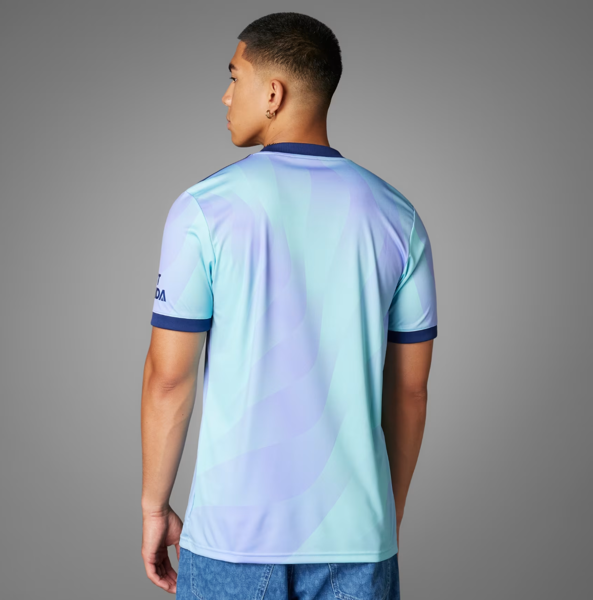 Screenshot_2024-09-18_194340_87106d75-b5b8-4f2a-ae38-7d60a27632d8 | UAE SPORT STORE Back view of a man wearing a pastel blue and lavender tie-dye T-shirt with navy sleeve cuffs, standing against a gray background