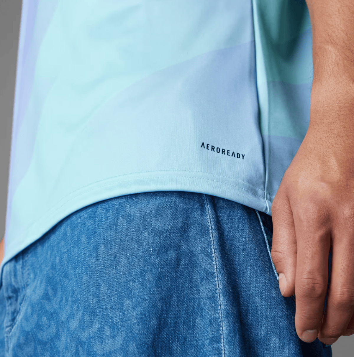 Close-up of a pale blue shirt hem with the 'AEROREADY' logo and blue denim jeans nearby.