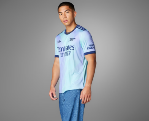Screenshot_2024-09-18_194428_3d551ac5-a7f2-4e14-a0a8-43cb49f4f38f | UAE SPORT STORE Man wearing a light blue Real Madrid jersey, standing in a neutral gray studio backdrop, facing slightly to the right.