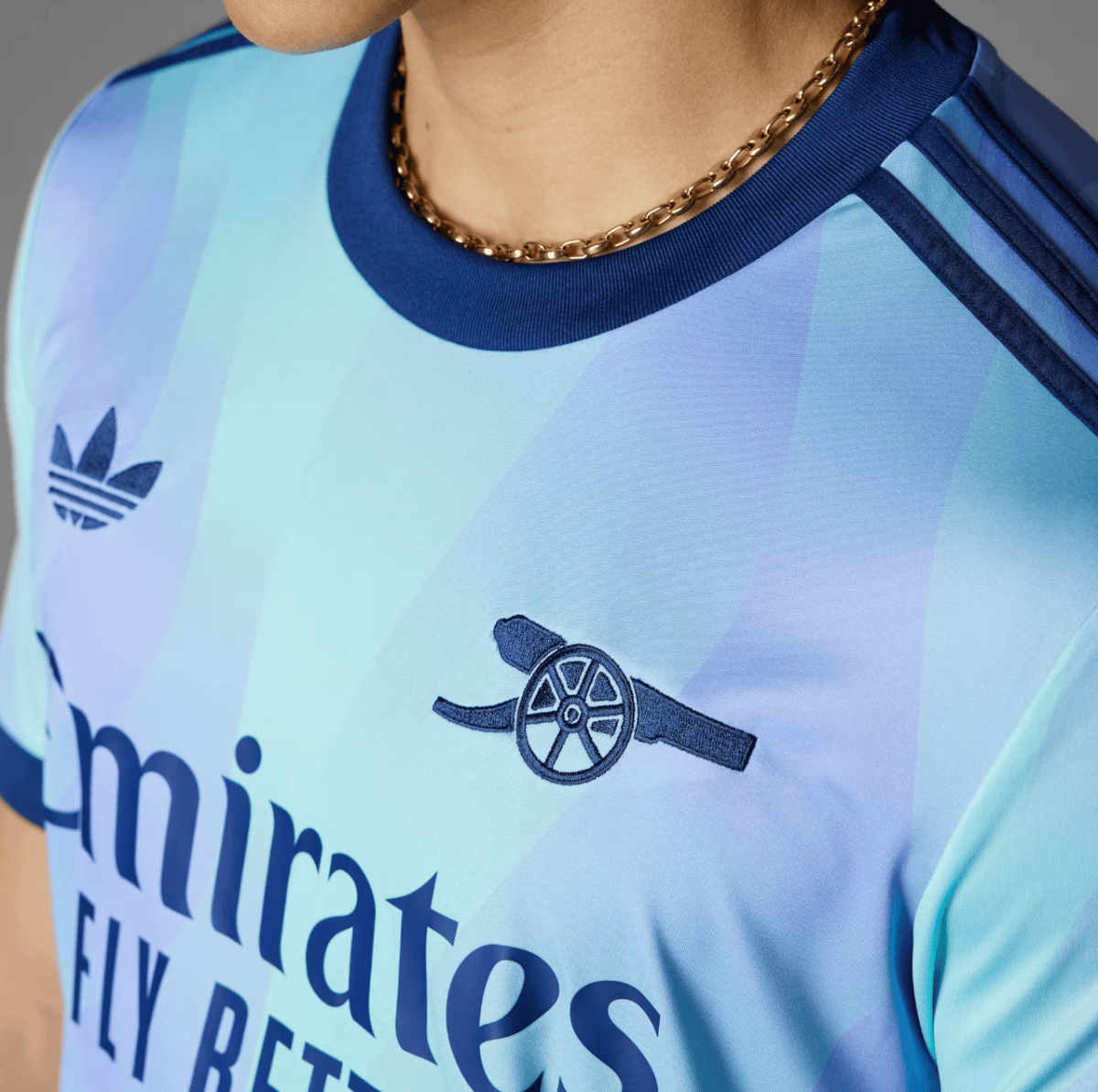 Close-up of a light blue gradient soccer jersey with an Adidas logo and a gold chain necklace visible at the collar.