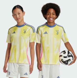 Two kids in bright yellow Juventus soccer jerseys stand side by side; one holds a soccer ball and smiles at the camera.