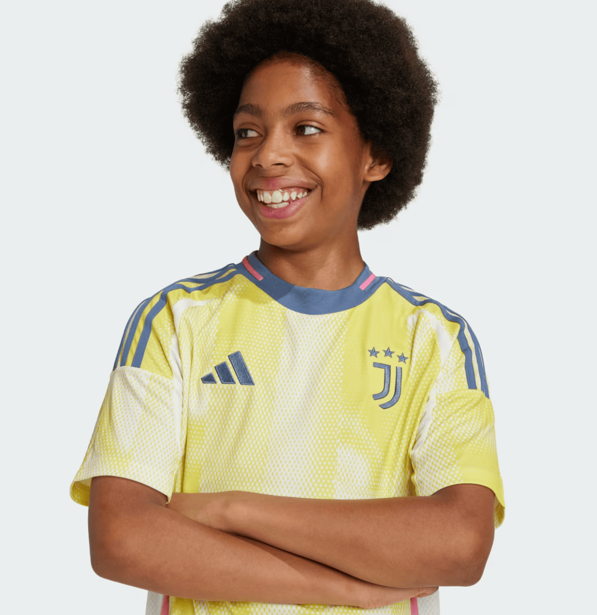 Young person with arms crossed, smiling, wearing a bright yellow Juventus soccer jersey with blue Adidas stripes.