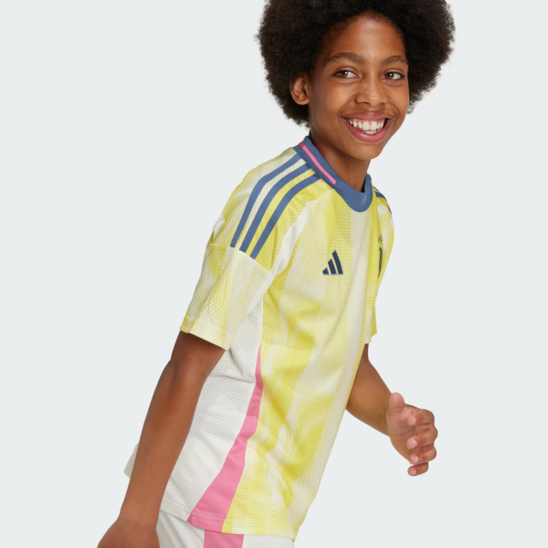 Young girl wearing a bright yellow Adidas soccer jersey with pink side panels, smiling while running against a light background.