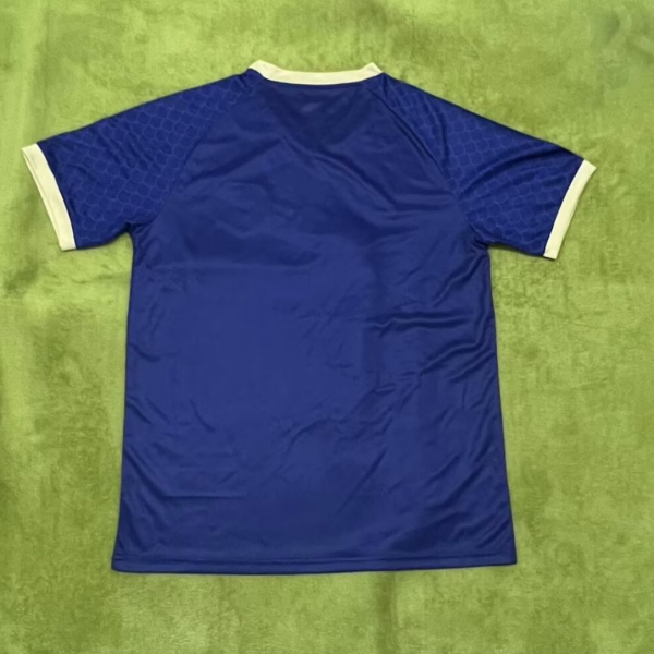 Blue athletic jersey with white collar and cuffs laid flat on a green surface, showing a honeycomb pattern on the sleeves.