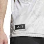 Close-up of a gray camo jersey hem with Adidas and Juventus logos patch on the side edge, subtle seam detail visible.