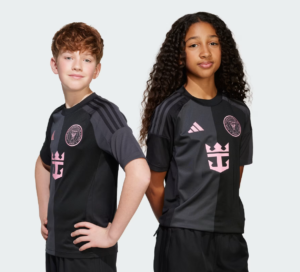 Two children pose in black and gray sports jerseys with pink crest and star-like logo on chest, standing against a light gray background.