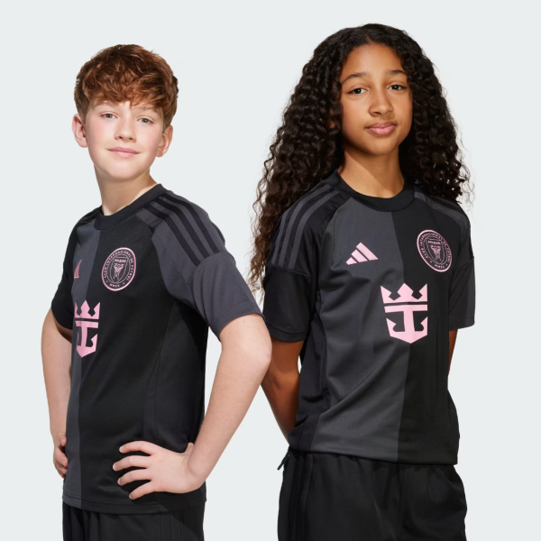 Two children pose in black and gray sports jerseys with pink crest and star-like logo on chest, standing against a light gray background.
